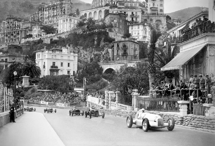 F1 cars racing past luxury yachts and buildings at the Monaco Grand Prix.